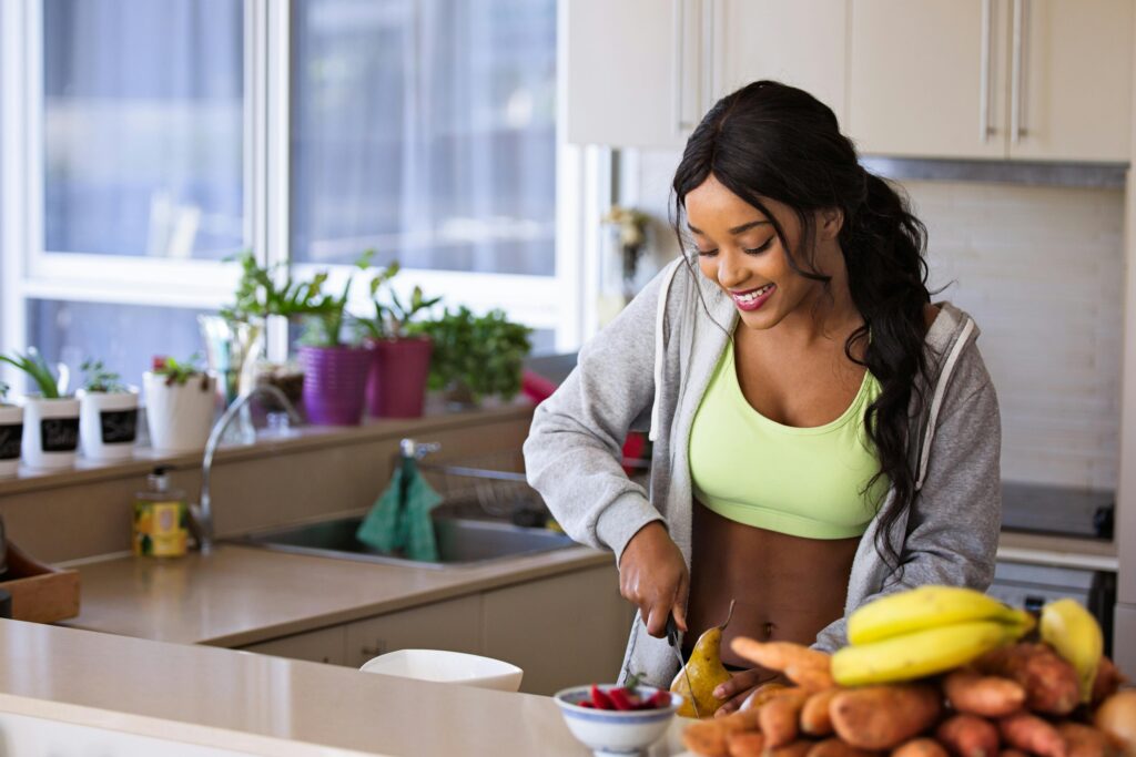 mkd wellness Smiling woman preparing fresh fruit in a sunlit kitchen, embodying a healthy lifestyle.